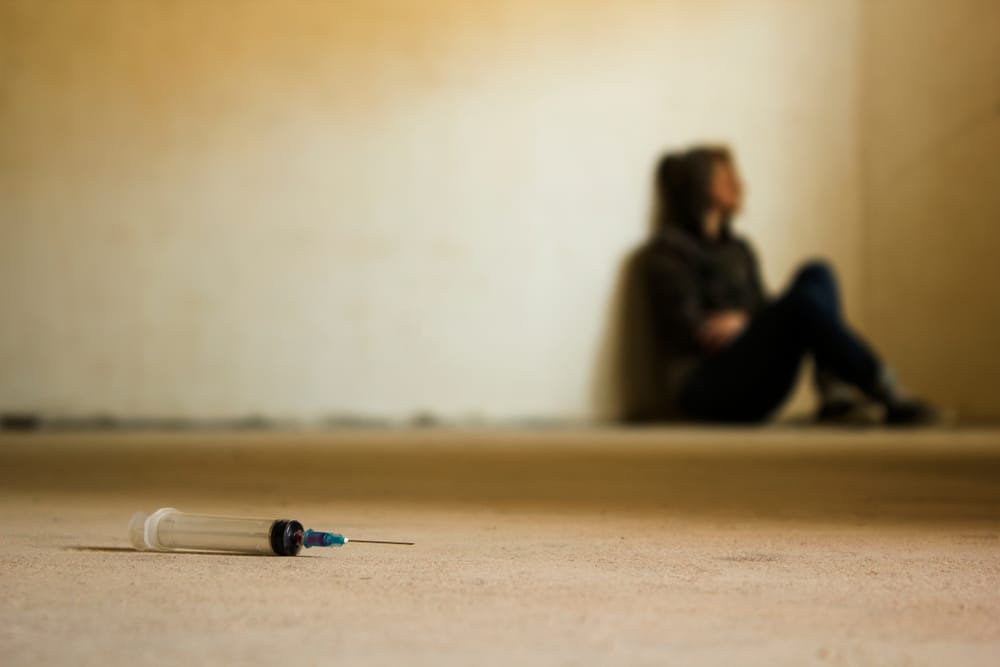 Teen sitting on the floor near syringe