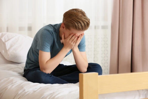 Depressed boy on his bed in need of help, suffering from addiction