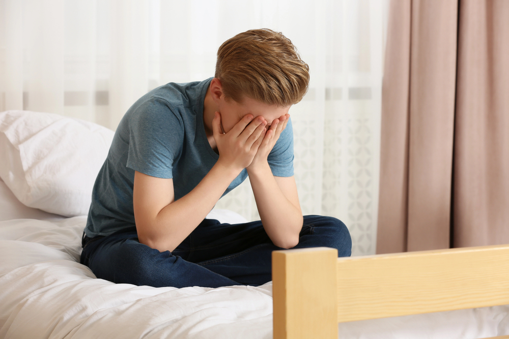 Depressed boy on his bed in need of help, suffering from addiction